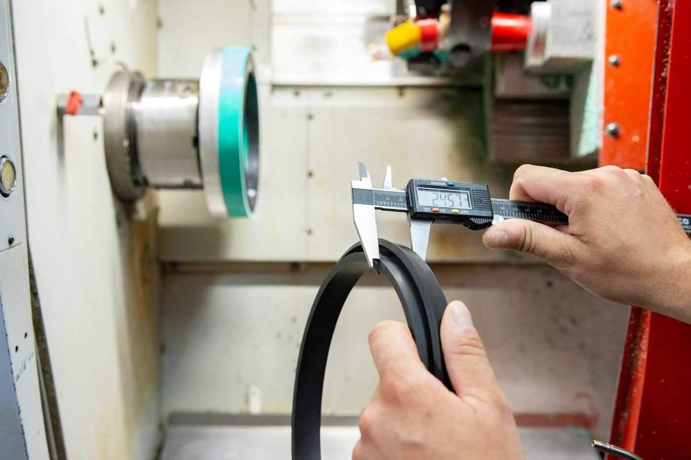 A technician measuring a gasket with a digital caliper beside the machine that made it